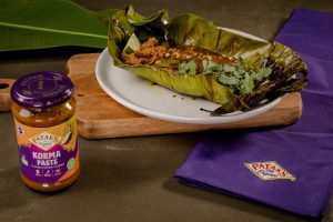 Korma spiced barramundi fillet cooked in a banana leaf parcel, unwrapped and garnished with fresh Thai basil, lemongrass and lime pickle