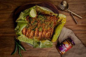 Vindaloo prawns wrapped and cooked in banana leaf parcels, served on a platter with fresh coriander, green chilli and lime wedges